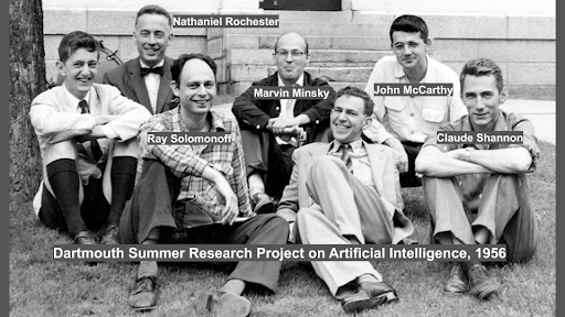 A photo of several early AI researchers, including Claude Shannon, Marvin Minsky and John McCarthy sitting in the grass at Dartmouth.